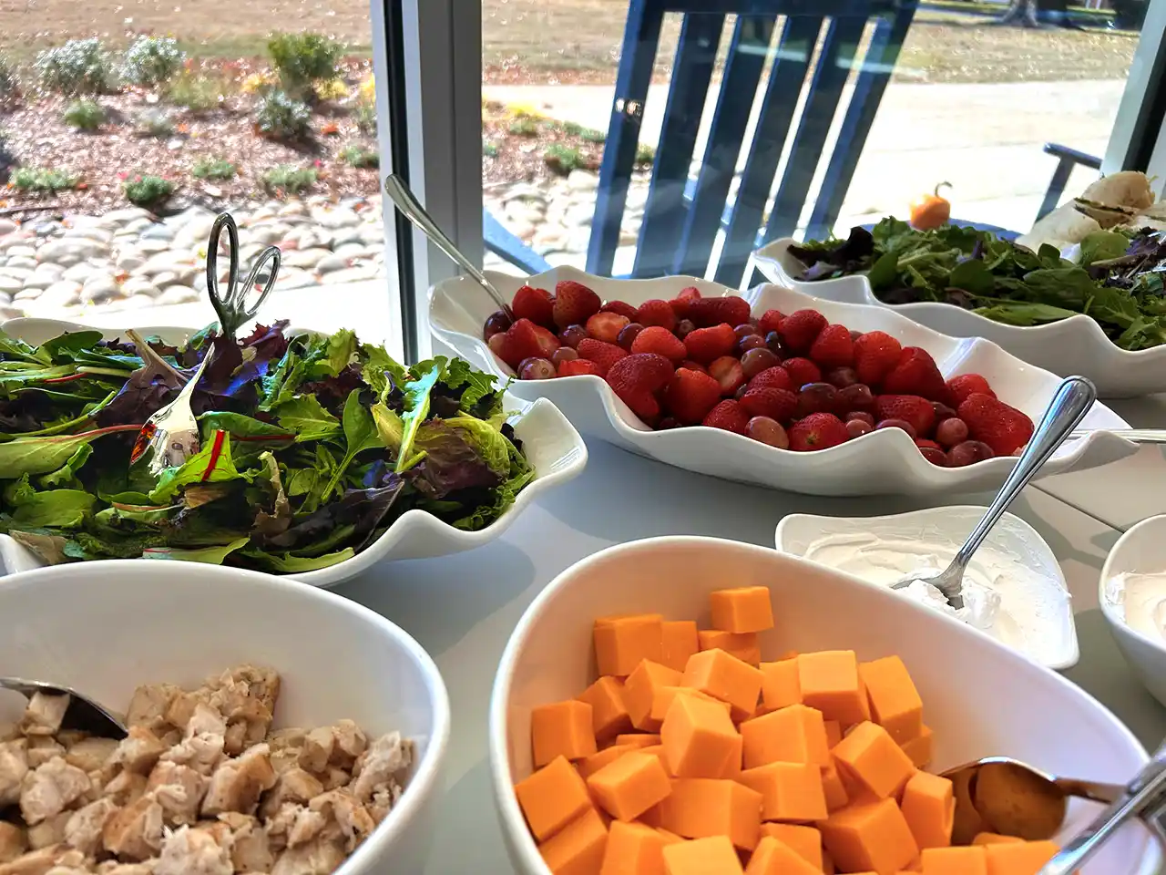 Catering spread with fresh salads, berries, cheddar cheese, and chicken for events