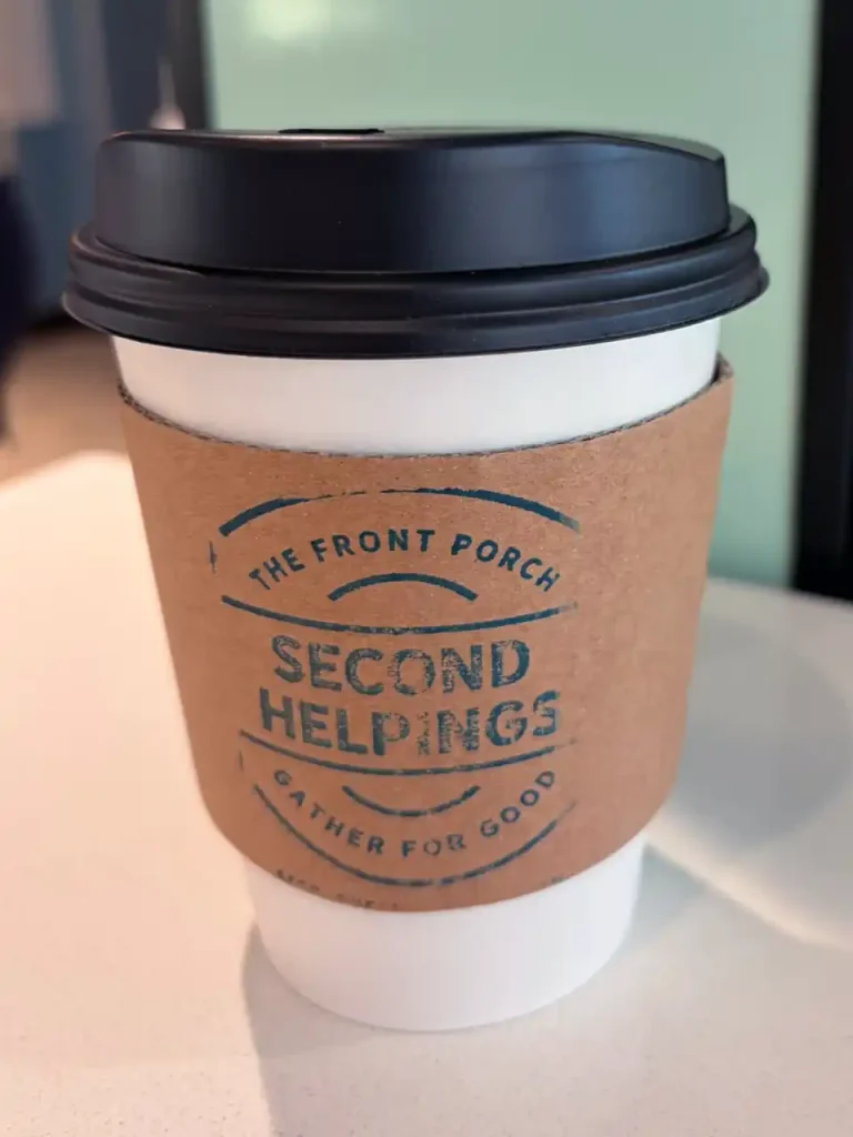 To-go coffee cup with recycled cardboard sleeve featuring the Second Helpings Café logo