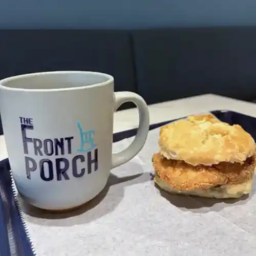 The Front Porch mug of coffee and a breakfast sausage biscuit on a parchment-lined tray